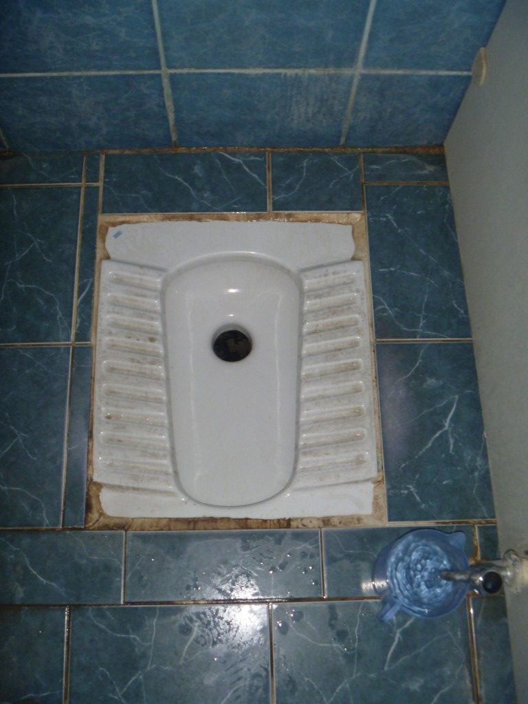 Typical squat toilet with a tap and a jug of water