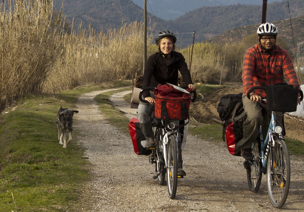 Annika und Roberto auf ihren Fahrrädern auf einem Feldweg. Neben ihnen ein Hund.